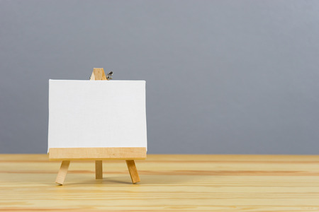 Easel with blank canvas on wooden table,Blank billboard on wood desk top with supplied bokeh...