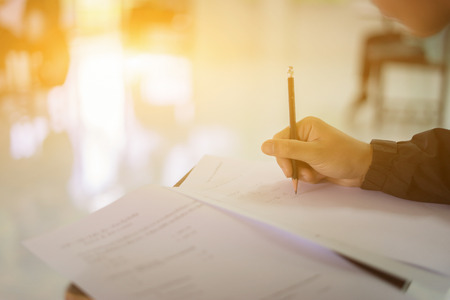 Student hand holding pen writing doing examination with blurred abstract background university  boy  in uniform attending exam classroom educational school:  college people in room vintage colorの写真素材