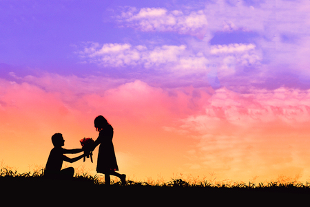 Proposal with a man silhouette asking for marry at sunset with the sun in the background, boquet of flowers kneeling and give engagement ring for his girlfriendの写真素材