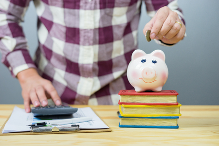 money, home, finance and relationships concept -man with pig bank sitting on desk,Businessman putting coin into the piggy banks,vintage color morning lightの写真素材