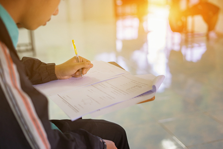 Student hand holding pen writing doing examination with blurred abstract background university boy in uniform attending exam classroom educational school: college people in room vintage colorの写真素材