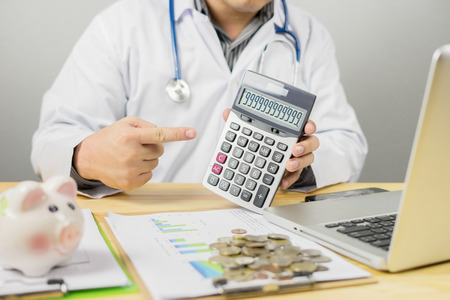 Young medical doctor caucasian healthcare professional wearing coat with stethoscope and prescription in hospital show and calculated on an electronic calculator for medical doctor fee,vintage colorの写真素材