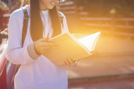 young girl student writes information from portable net-book while prepare for lectures in University campus and reading a book,vintage color,selective focus,education conceptの写真素材
