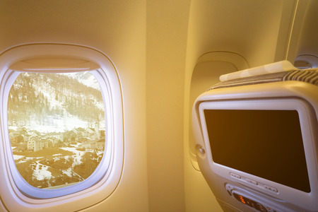 Sunrise ray light of Snow village on the alpine mountains as seen through window of an aircraft, plane interior touch screen ,vintage color selective focusの写真素材