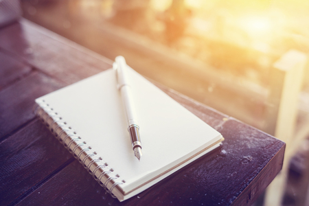 pen on the desk,Open a blank white notebook on wooden table and green bokeh background ,vintage color,selective focusの写真素材