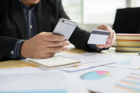 Man holding business card and dialing number at wooden desk,verifies account balance on mobile banking application.Online payment shopping,selective focus,vintage colorの写真素材
