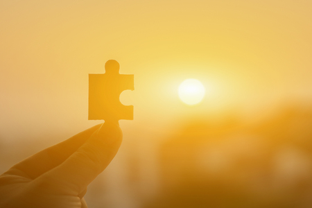 hands trying to connect  puzzle piece with sunset background. Jigsaw alone wooden   against sun rays. one part of whole. symbol of association and connection. business plan strategy conceptの写真素材