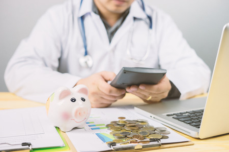 money in hospital finance relationships concept ,Doctor with piggy bank wanting payment Savings Pay Bill,Stethoscope financial checkup or saving medical insurance costs with a calculator,hight riskの写真素材