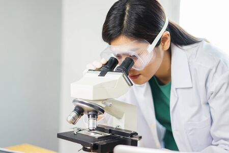 Female medical Doctor or research scientist looking through a microscope in a laboratory.science experiments,laboratory glassware containing chemical liquid for researching biology chemistry samples の写真素材