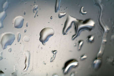 detail of roll off raindrops on glass in grey blurry backの写真素材