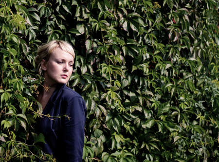  Beautiful  blonde caucasian young woman standing near the shrub and looks into the distanceの写真素材