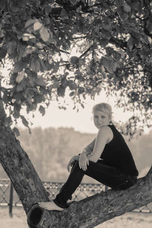 Beautiful Sadness young woman sitting on a tree branch and looks into the cameraの写真素材