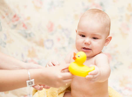 Baby crying in a yellow towel with toy sitting  on the floorの写真素材