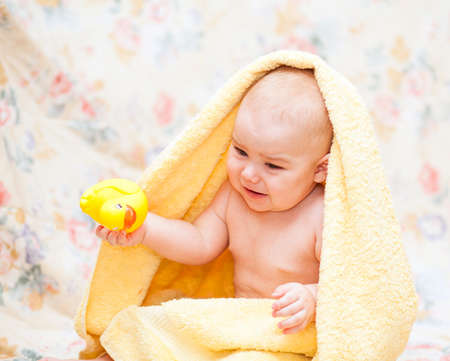 Baby crying in a yellow towel with toy sitting  on the floorの写真素材