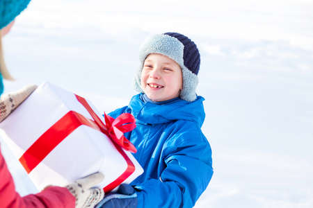 woman gives a Christmas present boy at nature with snowの写真素材
