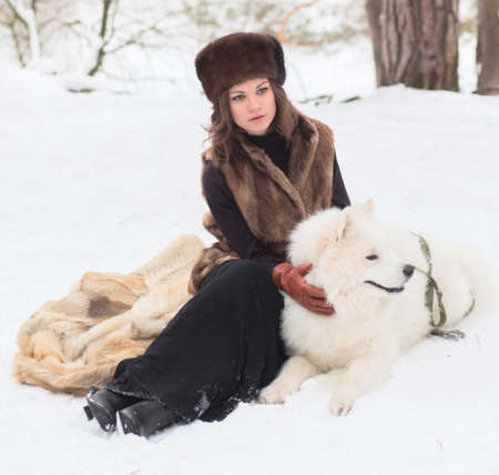 Girl in fur hat with samoyed dog in winter parkの写真素材