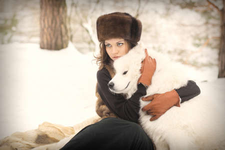 Girl in fur hat with samoyed dog in winter parkの写真素材