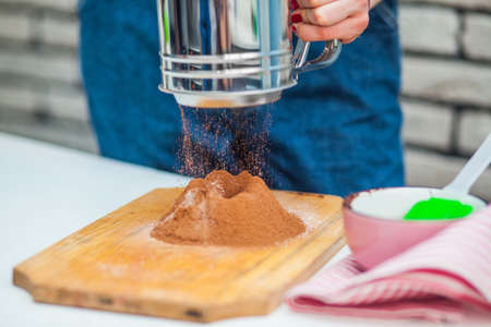 Hand sifts the flour and cocoa  through a sieve in the kitchenの写真素材