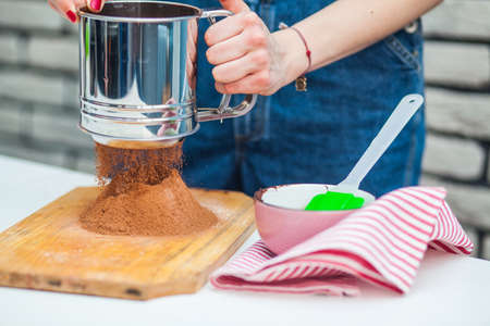 Hand sifts the flour and cocoa  through a sieve in the kitchenの写真素材