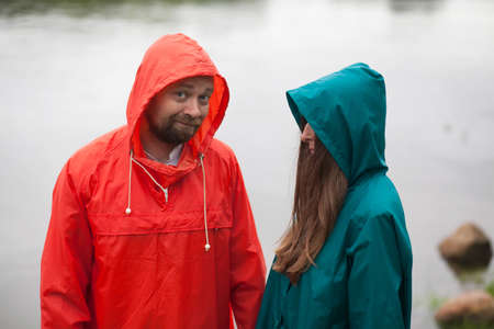 portrait of a man and woman with flowers, in raincoats, on the background of the river .の写真素材