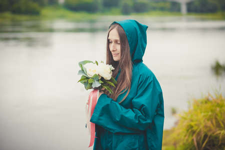 beautiful woman with flowers in raincoat on the background of the river .の写真素材