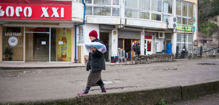 KUTAISI, GEORGIA - FEBRUARY 23, 2016: Woman carries goods walking on old street.のeditorial素材
