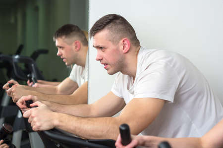 Young man and woman biking in the gym, exercising legs doing cardio workout cycling bikes.の写真素材