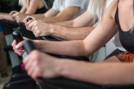 Young man and woman biking in the gym, exercising legs doing cardio workout cycling bikes.の写真素材