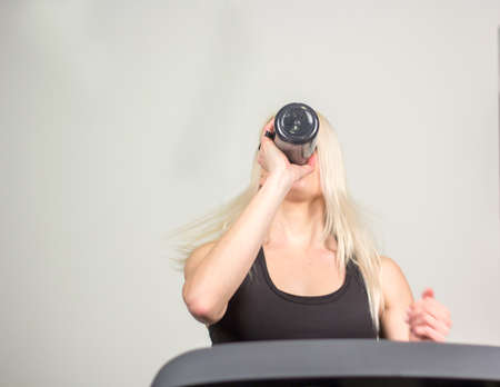 beautiful fitness girl running and drinking water on treadmill at the gym.の写真素材