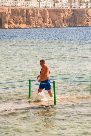 SHARM EL SHEIKH, EGYPT - JULY 9, 2019. a man walking in the sea on a background of hotels.