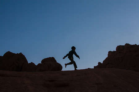 child silhouette running over the rocks in the desert at sunset.の写真素材