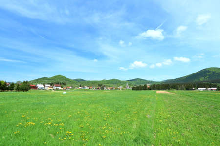 Green meadow and mountains under blue sky with white clouds in summerの写真素材