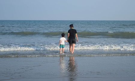 a mother and her son were walking on the beach with reflectionの写真素材