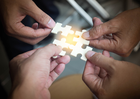 Group of business people assembling jigsaw puzzle wanting to put pieces of puzzle together on wood...