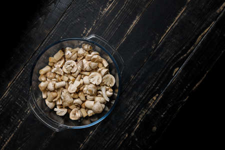 Cut forest champignons in glass bowl on black boards. Mushrooms on dark background.