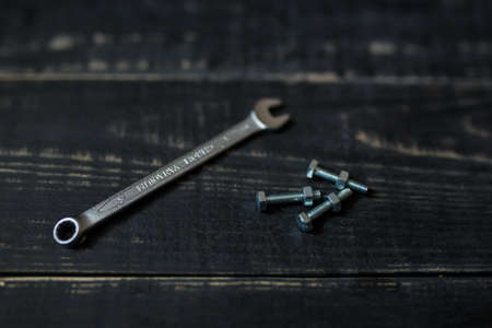 Double sided key, some nuts and bolts on black wooden background. Professional instruments, garage equipment, metal tools. Place for text.の写真素材