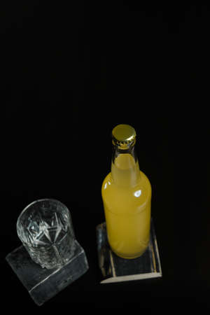Vertical shot of a bottle of orange juice, lemonade, alcoholic beverage and an empty glass standing on black wooden table.  Organic detox or unhealthy drinks concept. Place for text.の写真素材