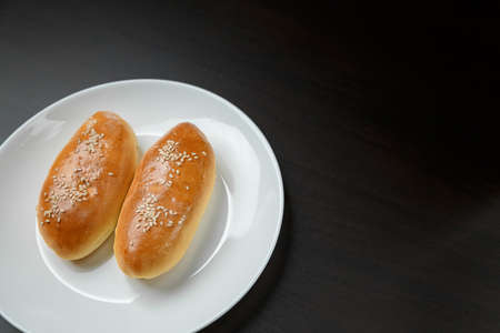 Delicious sesame buns or pies on white plate standing on black wooden table background. Tasty unhealthy snack for lunch or breakfast. Overweight, diet, nutrition, eating habits concept. Place for text.の写真素材