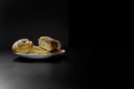 Delicious sesame buns or pies on white plate standing on black wooden table background. Tasty...