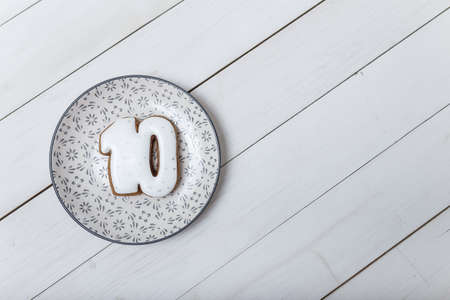 Number 10 shape gingerbread cookie on plate standing on white wooden table background. Number ten...