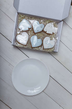 Present box and gingerbread cookies and empty white plate. Hearts shapes. Sweets on white wooden...