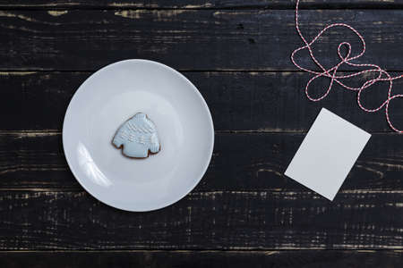 Sweater shape gingerbread cookie on white plate standing on black wooden table background....