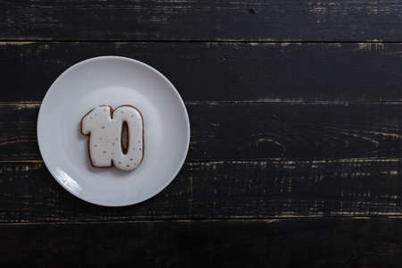Number 10 shape gingerbread cookie on white plate standing on black wooden table background. Number...