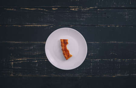 A small piece or bite of pie, leftover on white plate on black wooden table background. Tasty unhealthy product. Diet, nutrition, eating habits. Underweight or overweight concept. Copy space.の写真素材