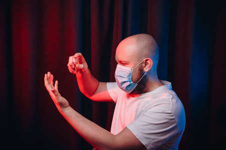 Man in gauze mask holding disinfection spray and sprinkling sanitizer on hands. Healthcare, respiratory illness prevention, prophylaxis of virus infections, COVID-19 concept.の写真素材