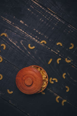 Brown wooden bowl or pot with pasta or raw macaroni on black wooden background, copy space....