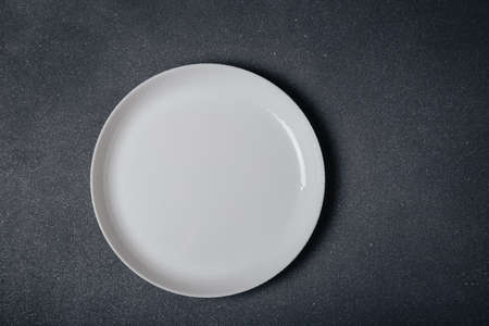 White round empty plate on dark gray background, top view, copy space. Waiting for dinner, food,...