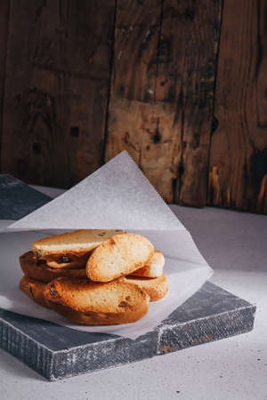 White wheat bread crackers, sweet croutons with raisins on paper, wooden table background. Tasty homemade appetizer. Vertical shot, copy spaceの写真素材