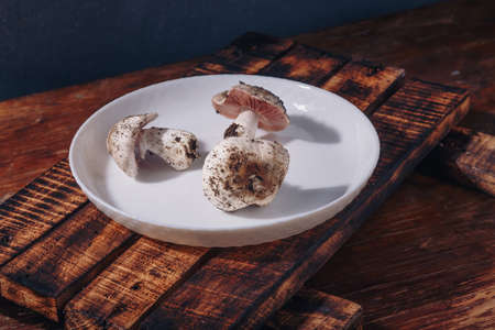 White plate with fresh raw champignons. Dirty forest mushrooms, preparing ingredients for cooking tasty homemade food. Close up shot.の写真素材