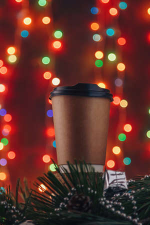 Christmas drink in eco friendly paper cup on blurry multicolored bright garland lights boke background. Coffee, cappuccino, latte, tea, hot beverages in disposable container. Vertical shot.の写真素材